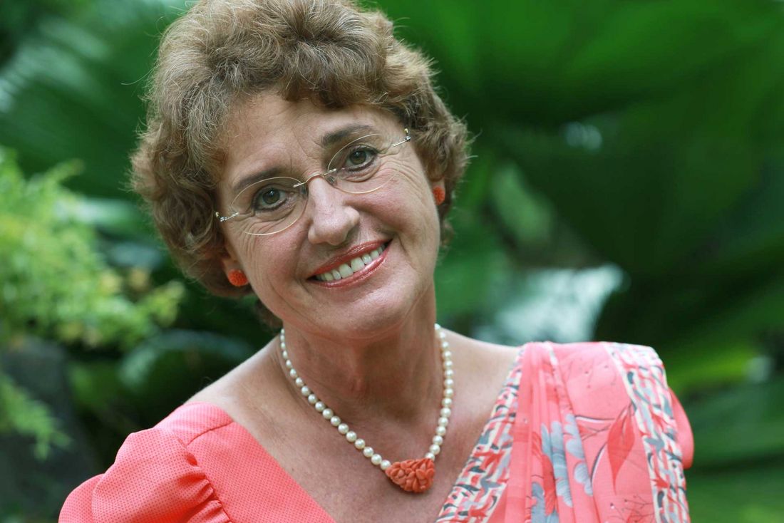 Ursula Beier im Gartenporträt, lächelnd, vor grüner Vegetation